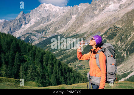 Frau hikerdrinks Wasser, stehend auf einem Berg im Hintergrund, Mont Blanc Massiv. Reisen rund um den Mont Blanc mit einem Rucksack. Stockfoto