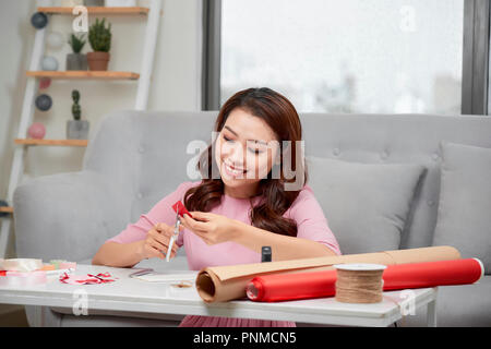 Lächelnde Mädchen schneiden valentine Herz aus rotem Papier mit einer Schere im Wohnzimmer Stockfoto