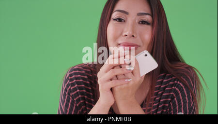 Asiatische Frau mit Telefon sitzen an der Kamera auf der Suche nach Green Screen Stockfoto