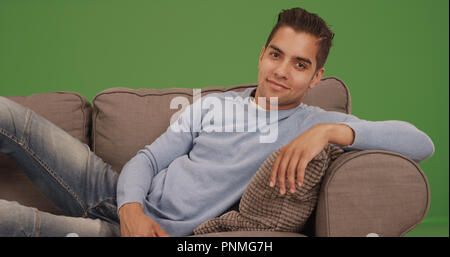 Portrait von hübscher junger spanischer Mann Festlegung auf der Couch auf der grünen Bildschirm Stockfoto