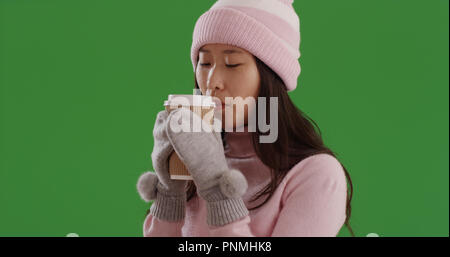 Kalte asiatische Frau in Winterkleidung sipping Kaffee Tasse auf Green Screen Stockfoto