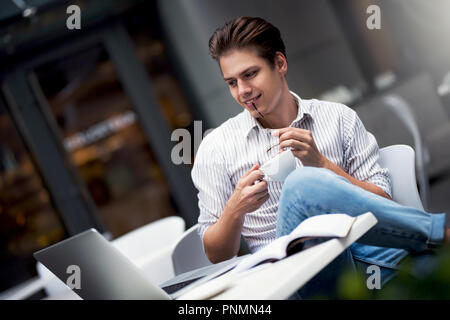 Stattlichen kaukasischen jungen Mann arbeiten am Laptop und lächelnd, während sie Kaffee im Cafe. Stockfoto