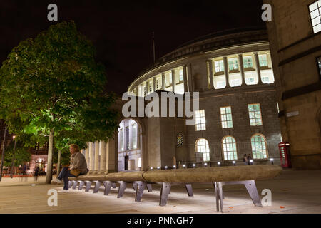 September 2017 - eine Frau sitzt in der Nacht auf einer beleuchteten Steinbank vor Manchester Central Library, die ikonische Gebäude im Zentrum von Manc Stockfoto