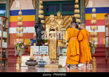 Zwei junge buddhistische Mönche in orangefarbenen Gewändern bewundern vergoldeten Statuen in einem Schrein in Phnom Penh, Kambodscha. Stockfoto