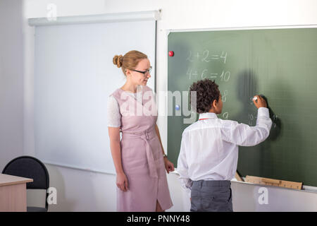 Junge Lösung von Addition und Subtraktion an Bord. Schüler schreiben Lösung der mathematischen Operation Stockfoto