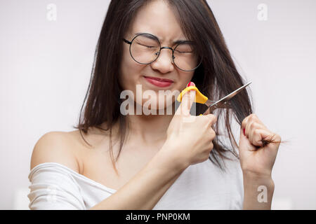 Asiatische Mädchen Probleme mit langen Haaren umgekippt, schneiden Split endet mit der Schere Stockfoto