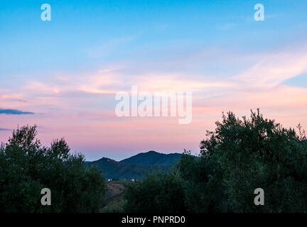 Axarquia, Andalusien, Spanien, 22. September 2018. Spanien Wetter: Wispy Wolken einen atemberaubenden Sonnenuntergang über die Axarquia Berge auf einem anderen heißen Tag erstellen. Einen Mandelbaum Grove schafft Silhouetten im Vordergrund gegen den Bergrücken Horizont Stockfoto