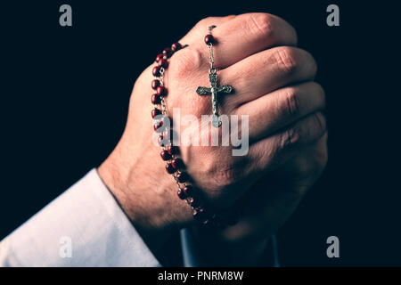 Männliche Hände halten einen Rosenkranz beten mit Jesus Christus am Kreuz oder Kruzifix auf schwarzem Hintergrund. Reifer Mann mit Christian katholischen religiösen Glauben Stockfoto
