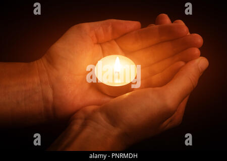 Hände halten und Schützen von leuchtenden leuchtet oder brennende Kerze Kerzenlicht auf die Dunkelheit. Schwarzen Hintergrund. Konzept für Gebet, Beten, hoffen, Vigil, Nacht Stockfoto