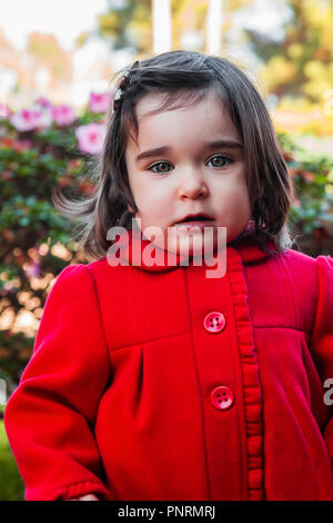 Niedlich, hübsch, fröhlich, lächelnd Kleinkind Baby Girl, mit einem frechen verspielten Lächeln mit eleganten roten Jacke oder Mantel. 18 oder 18 Monate alt Stockfoto