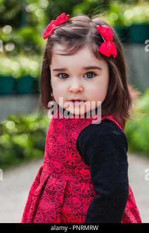 Niedlich, hübsch, fröhlich, lächelnd Kleinkind baby girl, Modellierung mit einem frechen verspielten Lächeln mit eleganten roten und schwarzen Kleid. 24 Monate alt Stockfoto