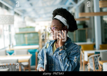 Hipster dunkelhäutige Frau mit Afro Frisur sprechen auf Smart Phone im Cafe. Stockfoto