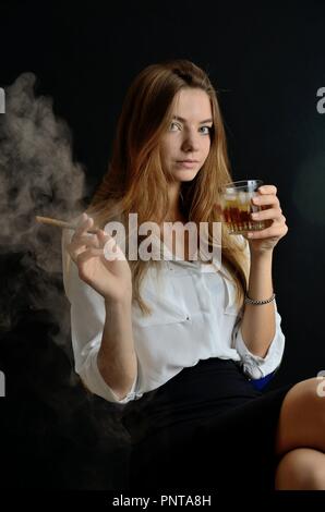 Junge Weibchen sitzt mit Zigarillo und Glas Whisky in der Hand. Elegante Frau mit weißer Spitze und schwarzen Kleid. Stockfoto