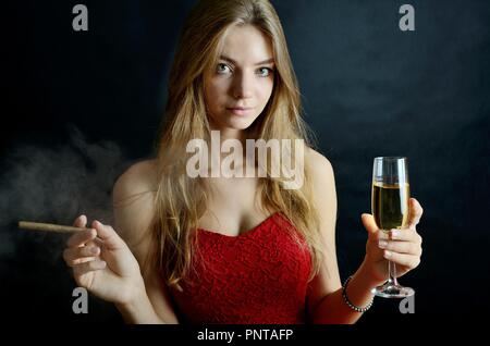 Junge Weibchen sitzt mit Zigarillo und Glas Weisswein in der Hand. Frau in rot Abendkleid. Stockfoto