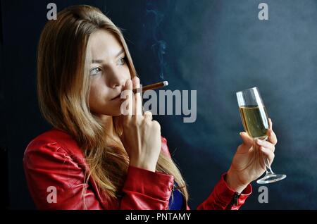 Junge Weibchen sitzt mit Zigarillo und Glas Weißwein in der Hand. Frau in der roten Jacke. Stockfoto