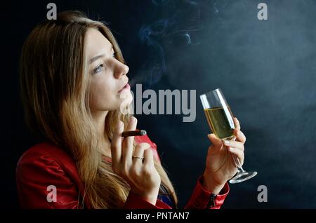 Junge Weibchen sitzt mit Zigarillo und Glas Weißwein in der Hand. Frau in der roten Jacke. Stockfoto