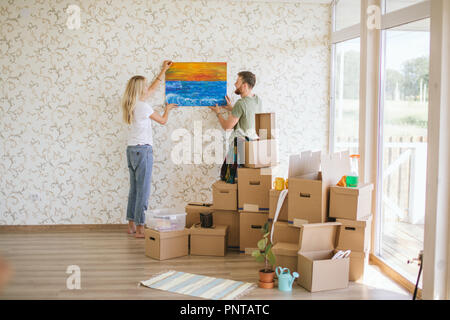 Umzug. Paar hängende Bild an der Wand im neuen Haus Stockfoto