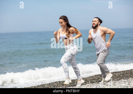 Glückliches Paar zusammen neben dem Wasser läuft am Strand Stockfoto