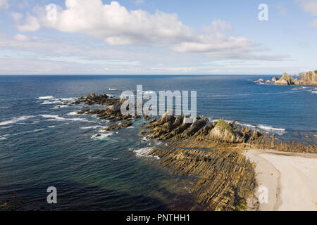 Gueirua Strand, Asturien, Spanien. Antenne allgemeine Ansicht, felsiger Strand mit Wellen brechen die Ufer und ein Paar in den weißen Sand sitzen. Stockfoto