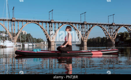 Yoga Lotus. Junge Frau Yoga am See auf einem Brett, sitzen in Lotus Stand Up Paddling Stockfoto