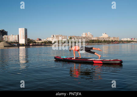 Stand Up Paddle Board Yoga von schönen Mädchen auf der helle Stadt Hintergrund durchgeführt, Yoga Ausbildung auf dem Wasser Stockfoto