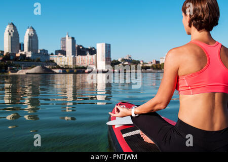 Stand Up Paddle Board Yoga von schönen Mädchen auf der helle Stadt Hintergrund durchgeführt, Yoga Ausbildung auf dem Wasser Stockfoto