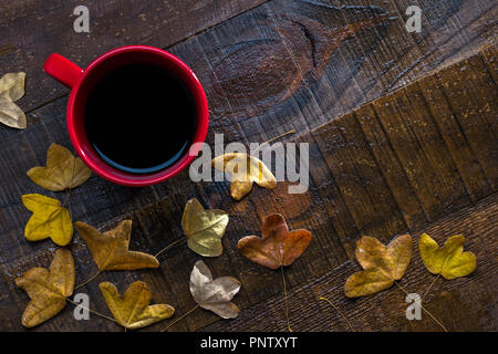 Rot Tasse schwarzen Kaffee und Blätter im Herbst auf alten nassen Holztisch. Flach Stockfoto