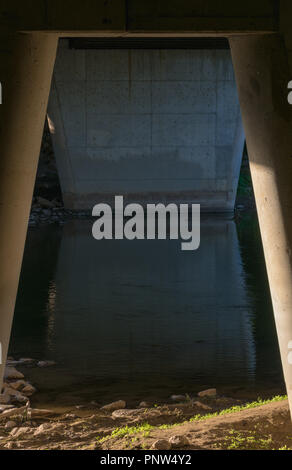 Ein Zement Unterstützung von einer Brücke als durch Säulen über eine langsame Strömung gesehen Stockfoto