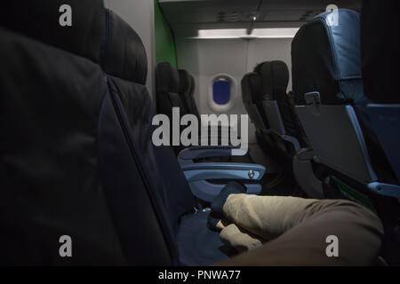 Nicht erkennbare Mann schläft auf Wirtschaft Sitze in einem Flugzeug. In der Nähe der Beine in Flugzeugen. Travel Concept Stockfoto