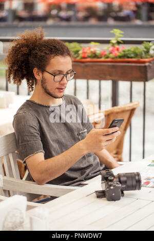 Guy reisender Planung Reise für Ferienhäuser mit Smartphone und Karte beim Sitzen im Cafe Stockfoto