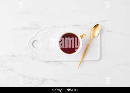 Blick von oben auf die weiße Tasse Tee mit goldenen Löffel auf bestreut servieren. Tasse Tee auf weißem Hintergrund. Flach mit kopieren. Stockfoto