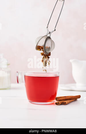 Früchte Tee in ein Glas Schale mit getrockneten Kräutern und Früchten fallen aus dem Tee-ei. Marmortisch Shirt, feminin mit rosa Hintergrund. Kopieren Sie Platz. Stockfoto