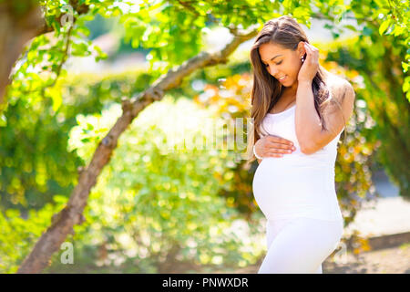 Schwangere Frau im Garten die Hand auf dem Bauch Stockfoto