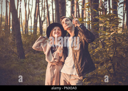 Junges Paar in Liebe umarmen im Herbst Wald. Mann nach oben zeigt. Glückliche Menschen gehen in Park Stockfoto