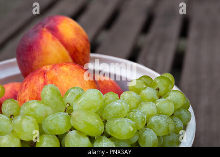 Pfirsiche und Trauben Bündel. Bunt Detail. Garten Tisch. Stapel der frische reife gewaschen Obst in der Schüssel. Gesund saftig vegetarischen Snack auf Holz- Hintergrund. Stockfoto