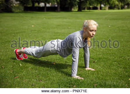 Blonde Frau in einem Trainingsanzug tun Drücken Sie ups und Excercising im Park Stockfoto