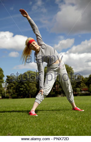 Blonde Frau in einem Trainingsanzug ausführen Stretching Übungen im Park Stockfoto