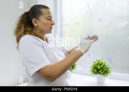 Krankenschwester hält eine Spritze, bereitet sich für eine Injektion, im Krankenhaus gegen das Fenster Stockfoto