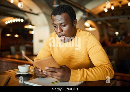 Schockiert junge afrikanische amerikanische Mann Eröffnung Mund, während auf seine Rechnung mit Kosten Stockfoto
