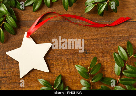 Sternförmige leer Weihnachtsgeschenk tag mit roter Schleife auf rustikalen Holz Hintergrund mit natürlichen Evergreen Dekorationen. Einfache urlaub Papier basteln. Stockfoto