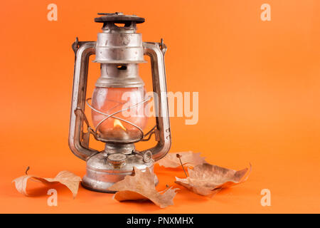 Alten retro gas Laterne mit brennenden Licht und gefallene Laub auf orange Hintergrund isoliert. Herbst Konzept. Close Up, selektiver Fokus Stockfoto