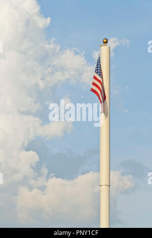 Eine amerikanische Flagge hängt von der Spitze eines Mastes mit einem hoch aufragenden, zerlumpten Cumulus Wolke und blauer Himmel im Hintergrund. Stockfoto