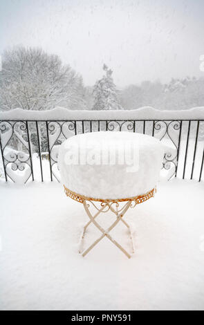 Metall Tisch eines Gartenmöbel Terrasse in tiefem Schnee im Winter in einem Garten in Surrey, Großbritannien mit Blick auf verschneite Bäume durch Geländer Stockfoto