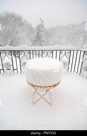 Metall Tisch eines Gartenmöbel Terrasse in tiefem Schnee im Winter in einem Garten in Surrey, Großbritannien mit Blick auf verschneite Bäume durch Geländer Stockfoto