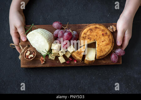 Käseplatte mit verschiedenen Käsesorten, Trauben, Nüsse und Hände der Käser auf schwarzem Hintergrund. Italienischen Käse und Obstteller. Stockfoto