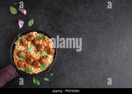 Spaghetti Nudeln mit Hackfleischbällchen, Tomatensauce und frischem Basilikum in gusseisernen Pfanne. Gesunde hausgemachten italienischen Teigwaren auf rustikalen schwarzer Hintergrund mit Kopie spa Stockfoto