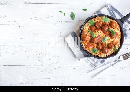 Spaghetti Nudeln mit Hackfleischbällchen, Tomatensauce und frischem Basilikum in gusseisernen Pfanne. Gesunde hausgemachten italienischen Teigwaren auf weißem Holz- Hintergrund mit Kopie spa Stockfoto
