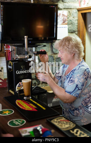 Lady gießen ein Pint Guinness in den Pub The Abbey House im Vordergrund, Castlepollard, Co Westmeath, Irland genannt Stockfoto