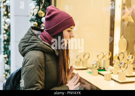 Eine junge schöne Frau oder ein Mädchen schaut durch ein Schaufenster während der Weihnachtsferien und ist überrascht. Stockfoto