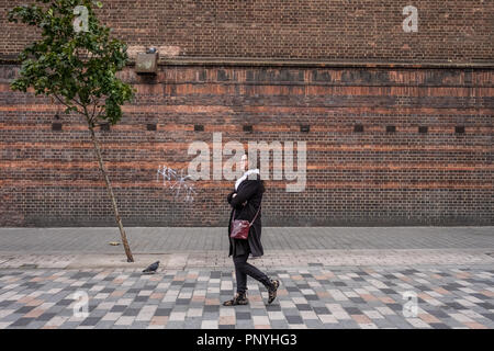 Eine einsame Person an einem einsamen Baum an einem windigen Tag in London. Stockfoto